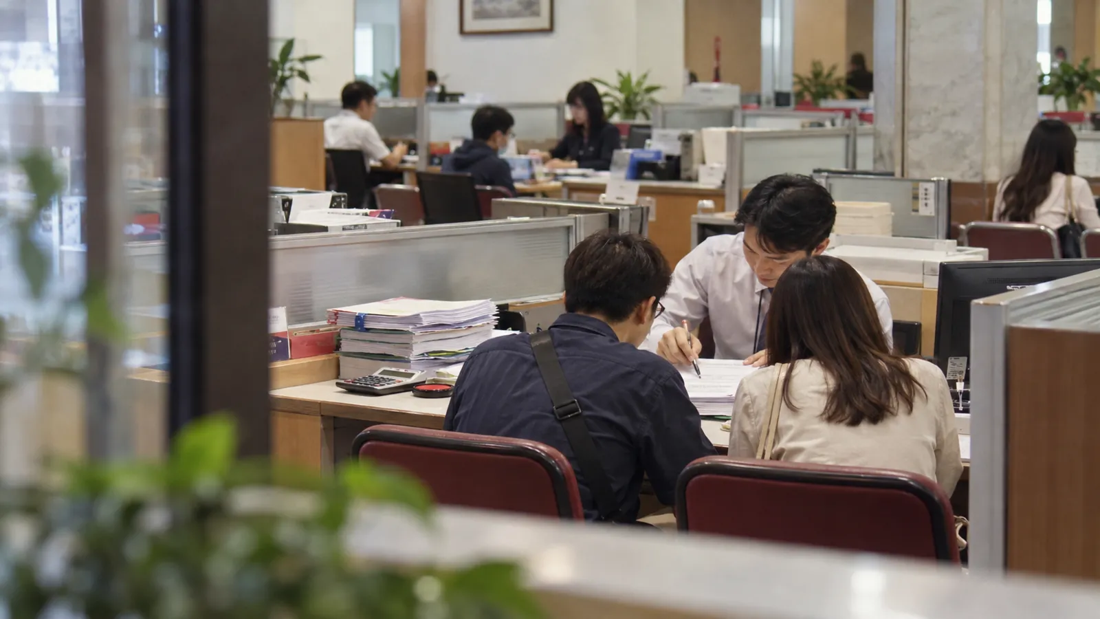 民眾在銀行櫃檯與專員核對文件,審慎規劃房貸申辦時程。